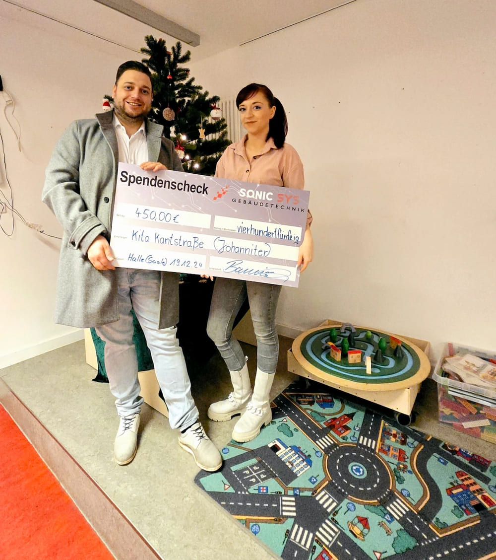 Roy Banisch überreicht einen großen Spendenscheck über 450€ an eine Mitarbeiterin der Johanniter-Kita in der Kantstraße